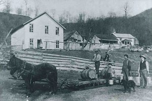 An old photo of the Silas Sharp homestead and first store. Creola stands in doorway with big sister Ada or Violet. L.D. on sled, Ivan at his side, two farmhands unknown.  Person on horseback is riding up the road.